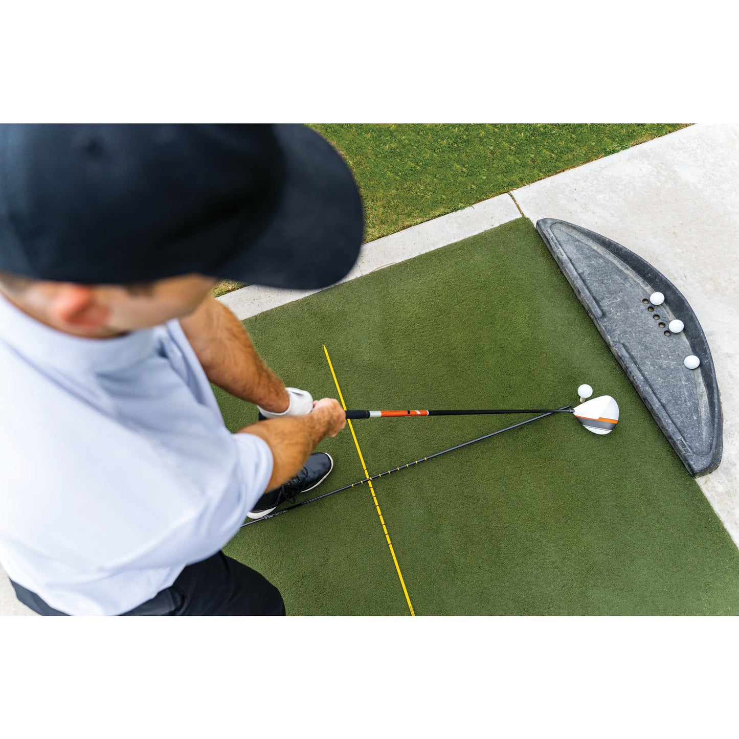 Golfer practices tee shot on artificial turf with golf ball and club near a golf bag on a golf course
