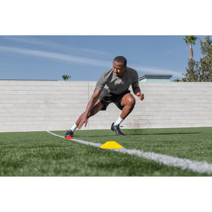 Athlete places a cone on the ground during training on a grass field under a blue sky