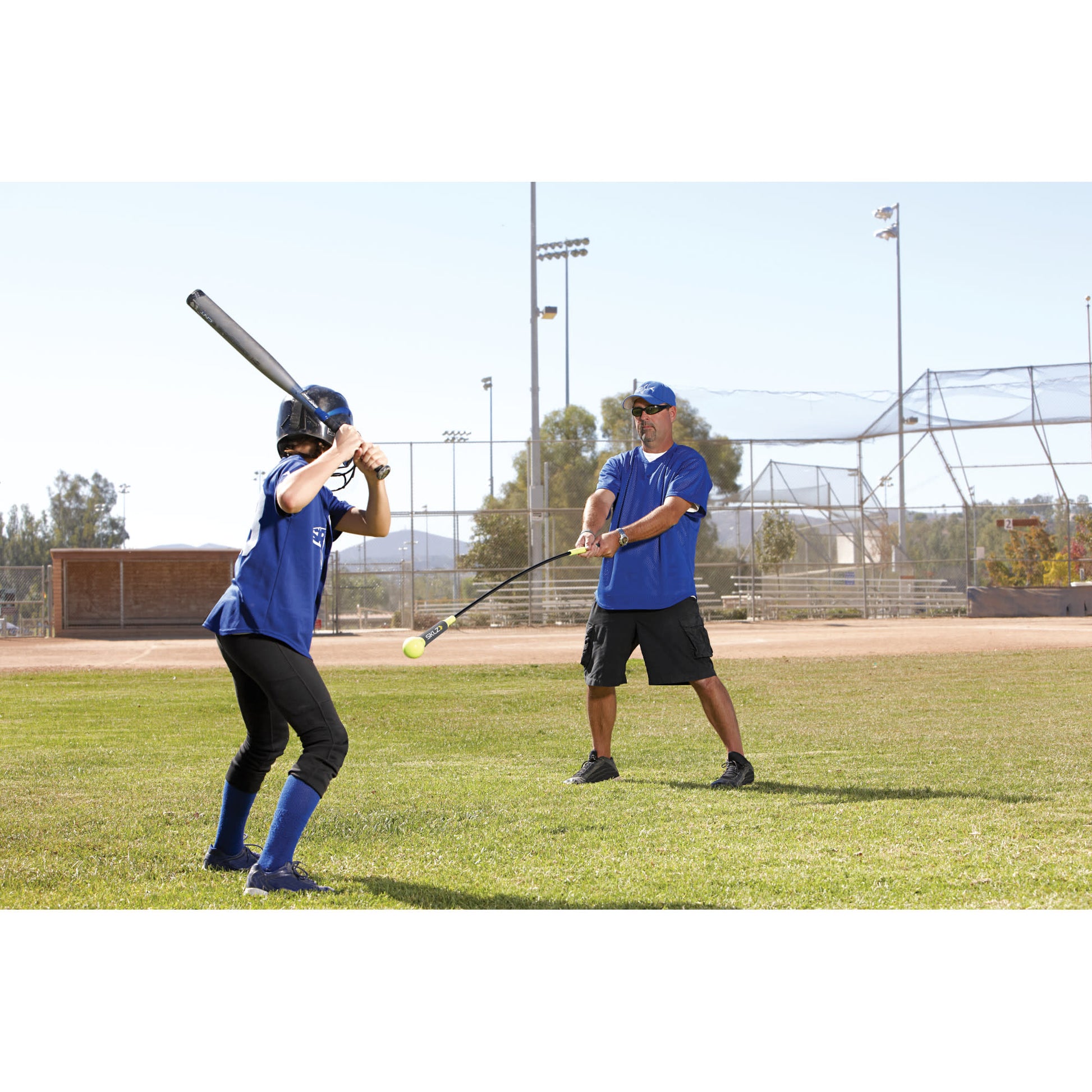 Player swings bat at ball during practice on a baseball field with coach watching