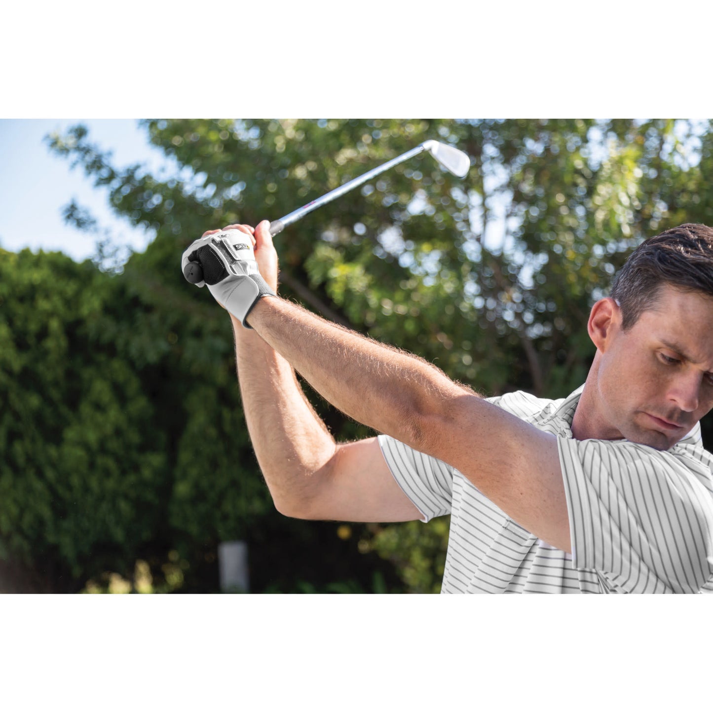 Golfer swings a club on a golf course during daytime with trees in the background