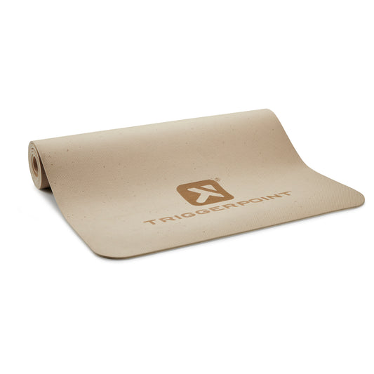 A beige yoga mat with a Tiggerpoint logo lies partially rolled on a white surface