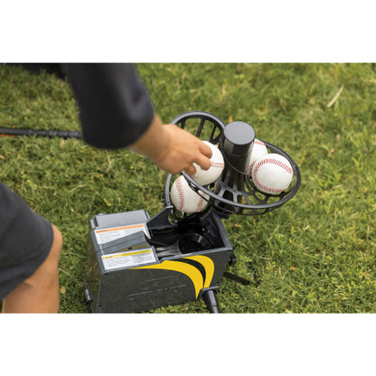 Person loads baseballs into a pitching machine on green grass field.