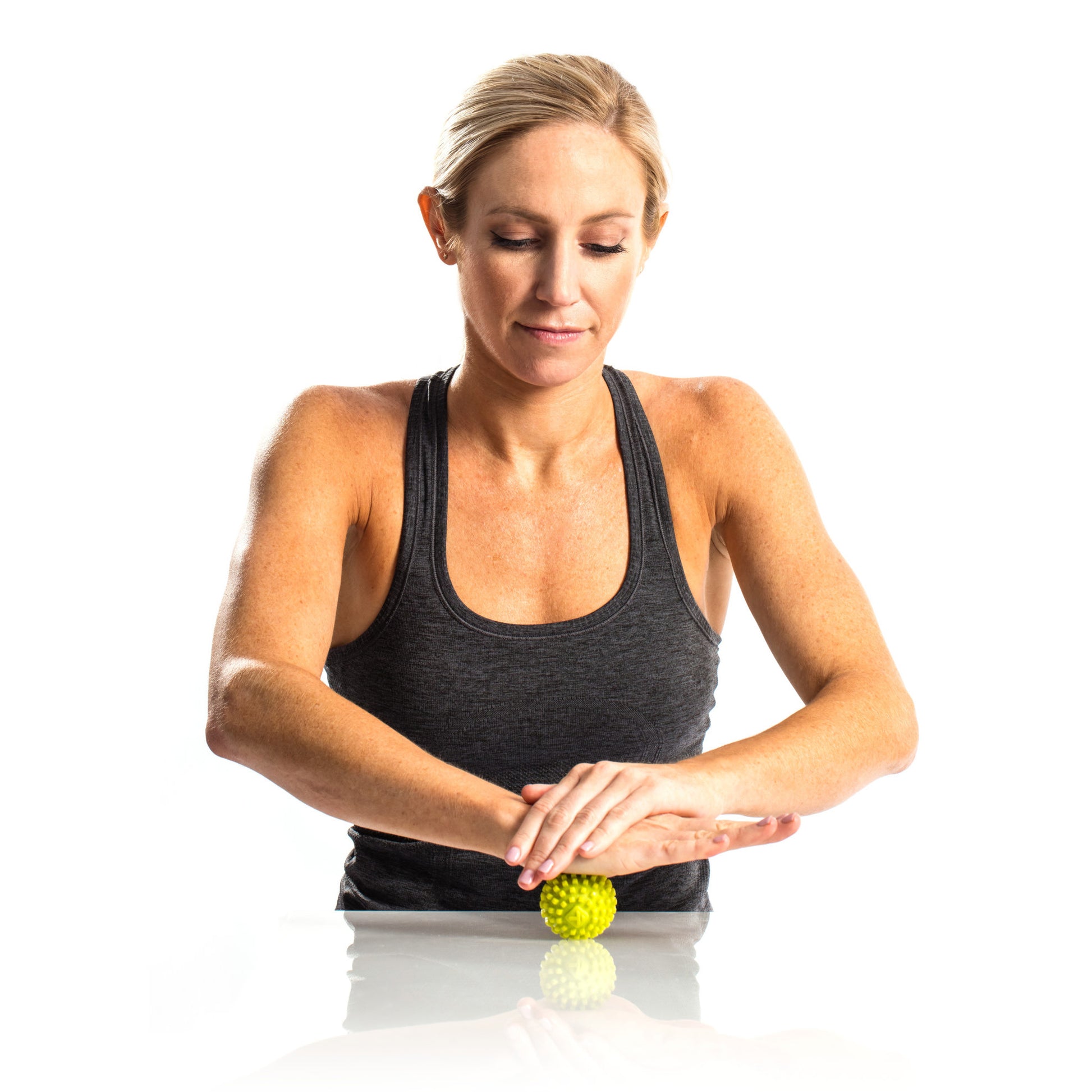Woman rolls a massage ball on a reflective surface against a white background