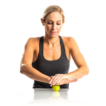 Woman rolls a massage ball on a reflective surface against a white background