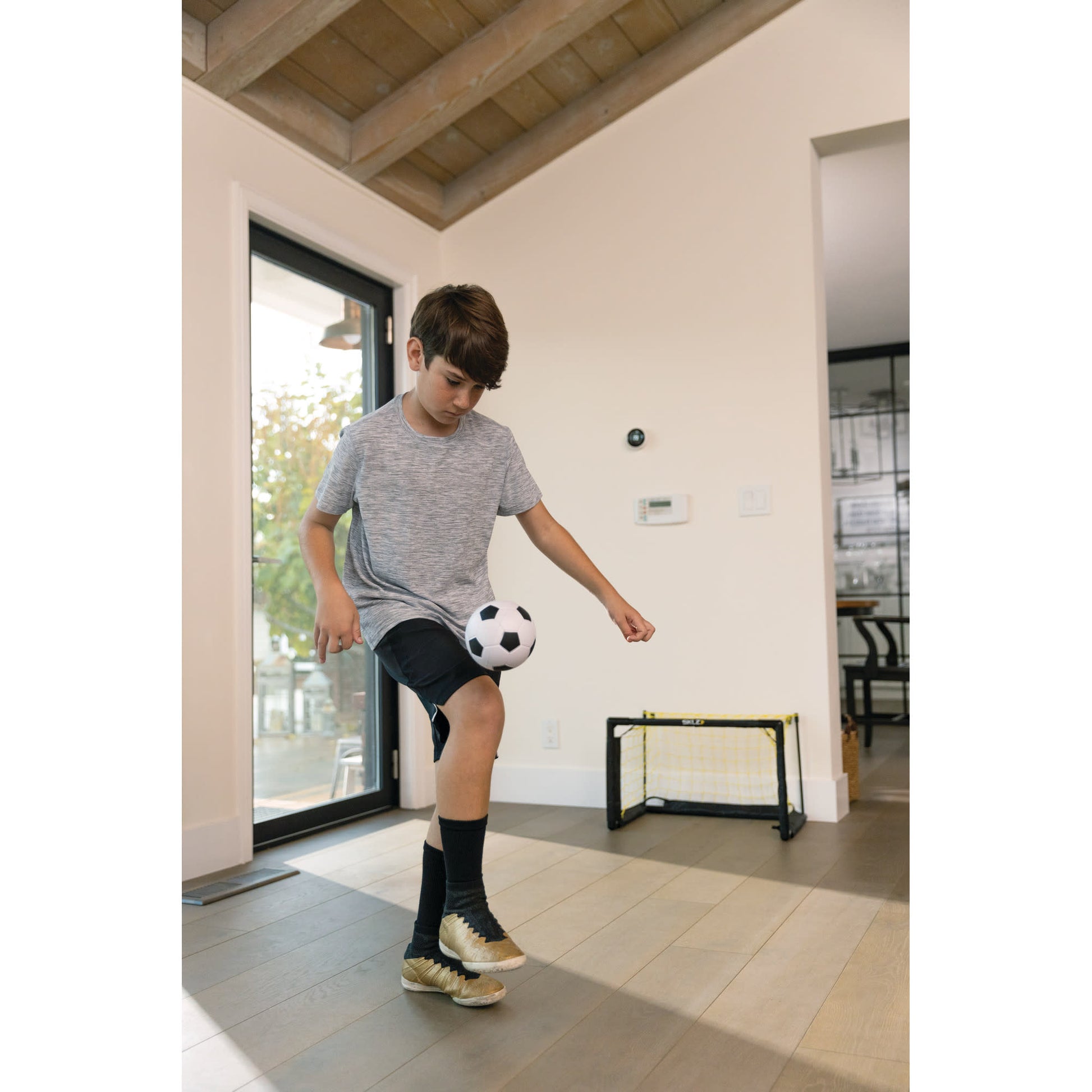 Boy kicks soccer ball inside a room with a small goal against a white wall