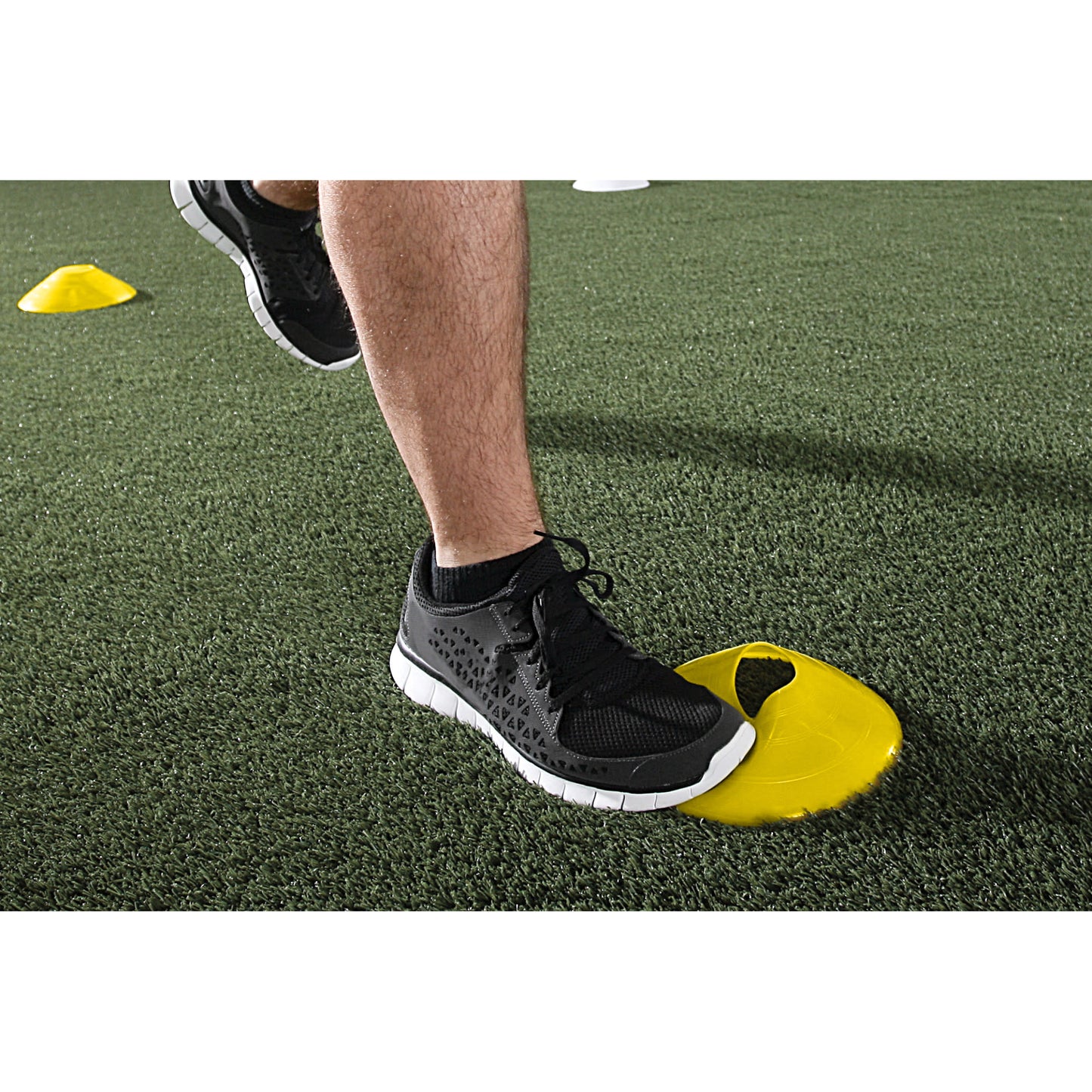 A persons foot presses on a yellow training cone on artificial turf during agility drill