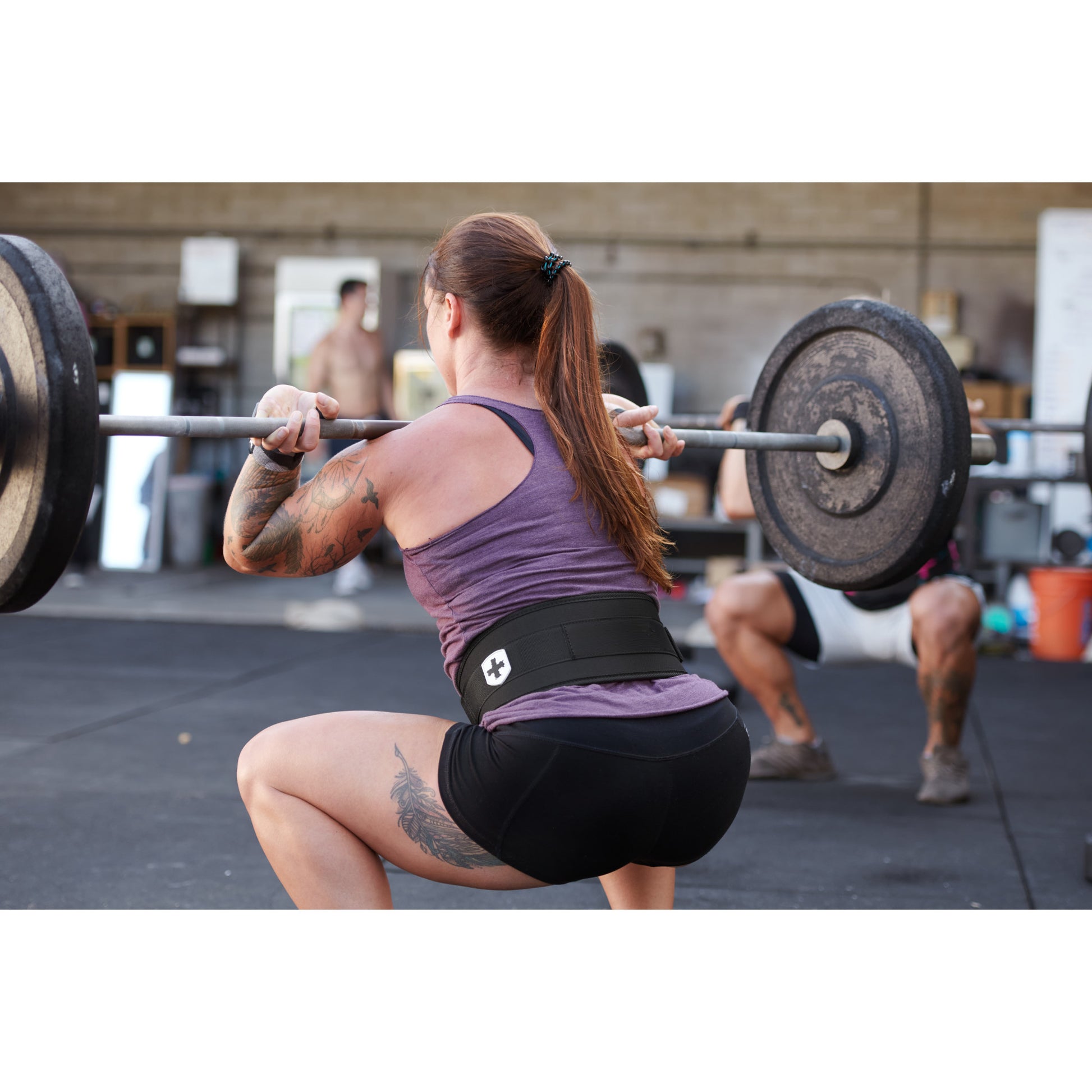 A person squats with a barbell inside a gym, wearing a weightlifting belt.