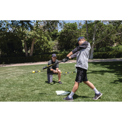 Boy practicing baseball swing with coach on grassy field in a park