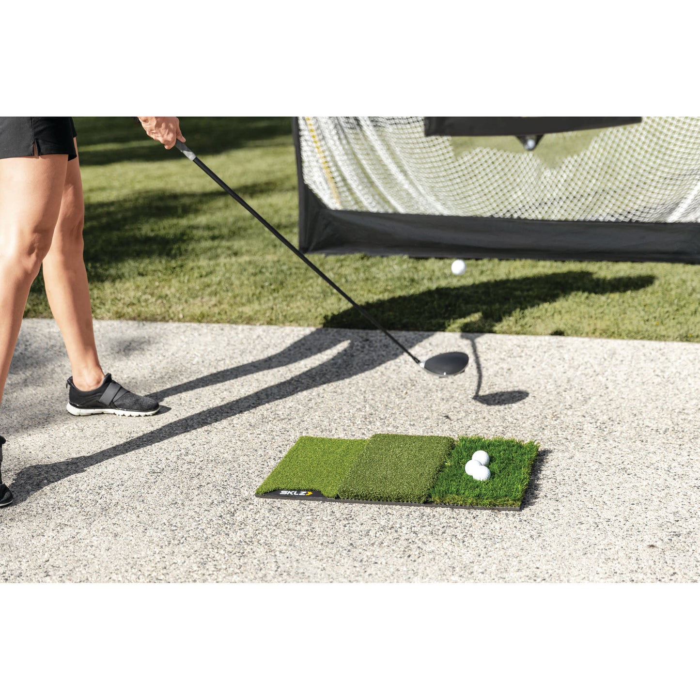Golf club hits golf balls on a mat in an outdoor practice area near a net