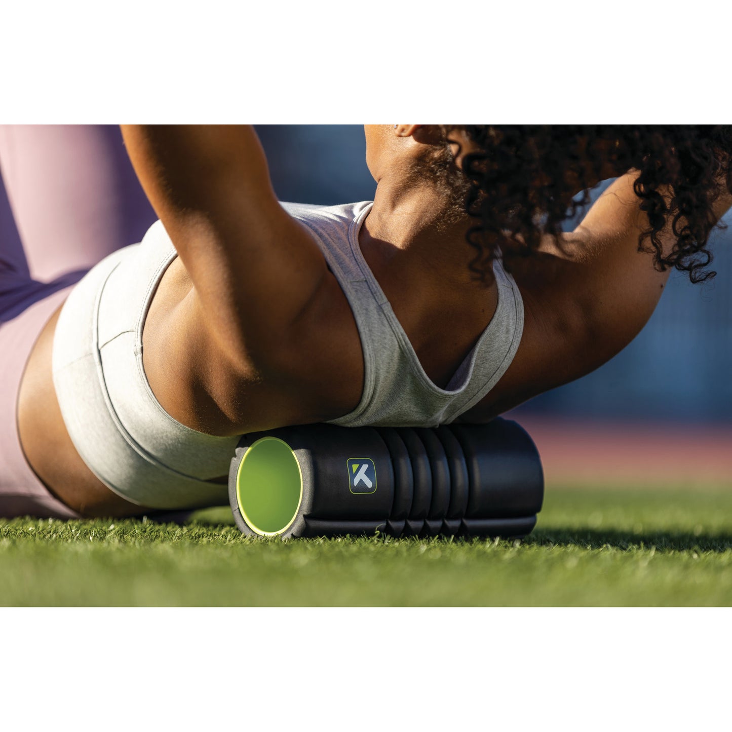 A person uses a foam roller on their back outdoors on a grassy field.