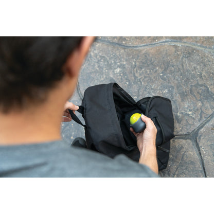 Person stores gym ball in backpack outside on stone surface