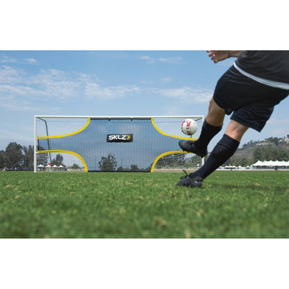 Soccer player kicks a ball toward a goal during practice on a grass field under a blue sky