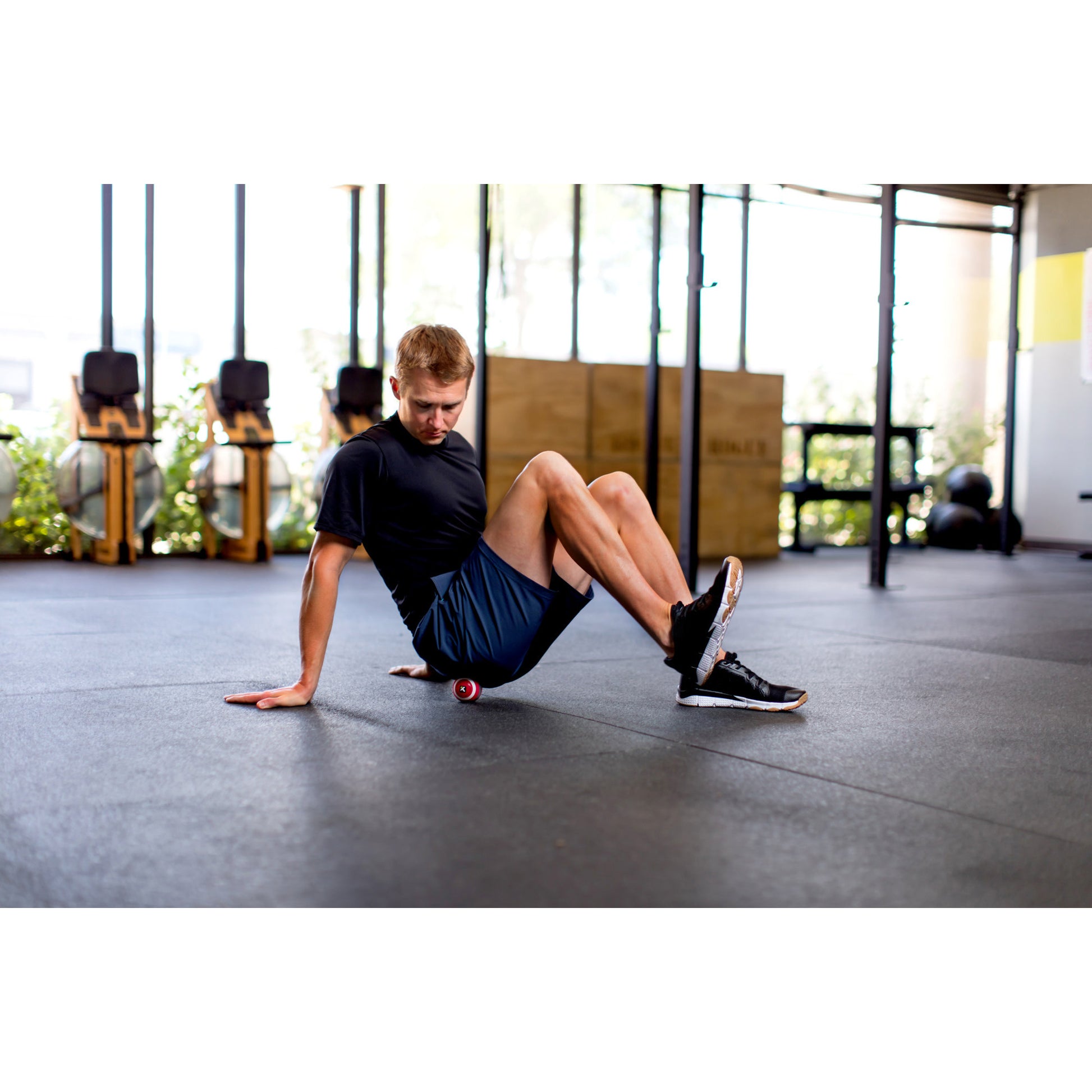 Man uses foam roller on leg muscles in a gym for muscle recovery and flexibility.