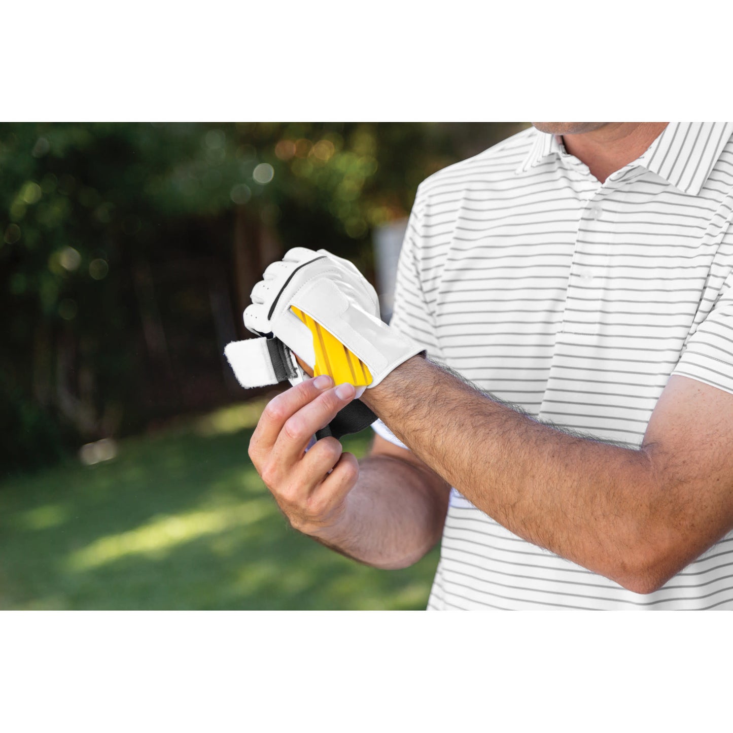 A person puts on a golf glove outdoors in a park or yard setting