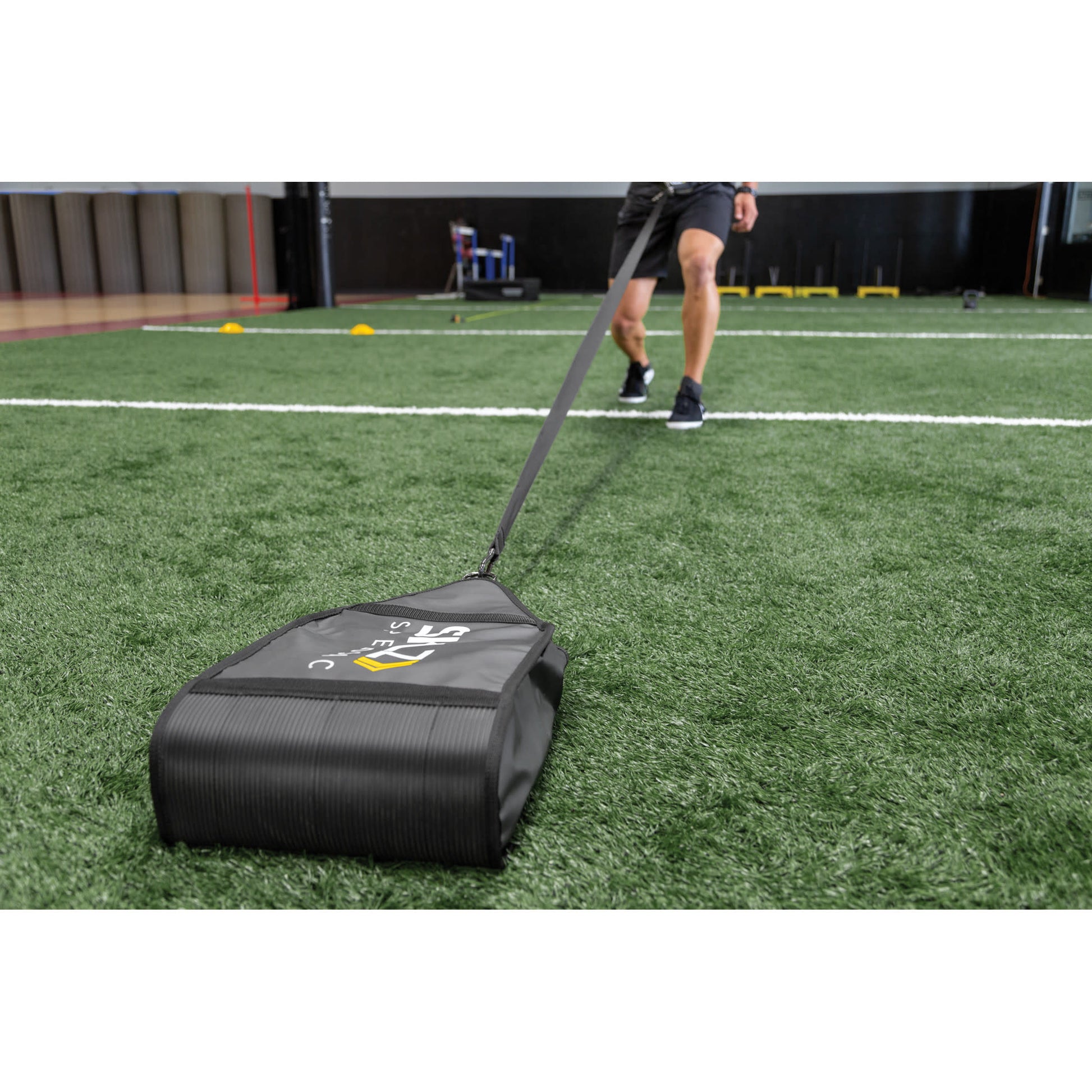 A person pulls a sled on artificial turf during training at an indoor sports facility