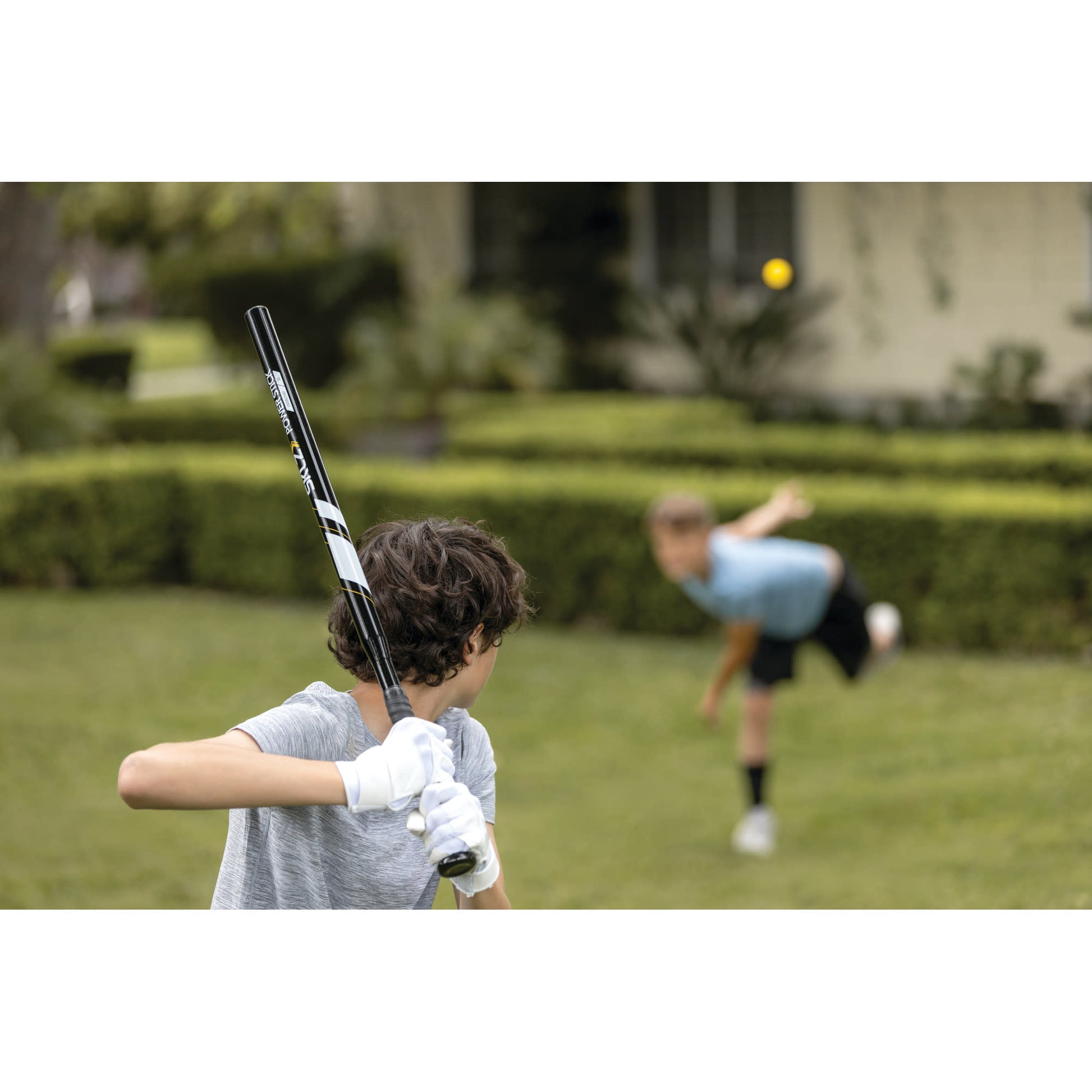 Kids play baseball outdoors with a bat and ball on a grassy field