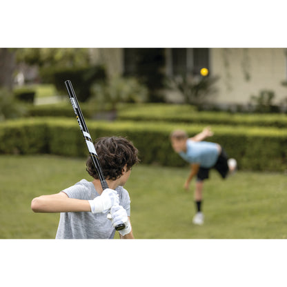 Kids play baseball outdoors with a bat and ball on a grassy field