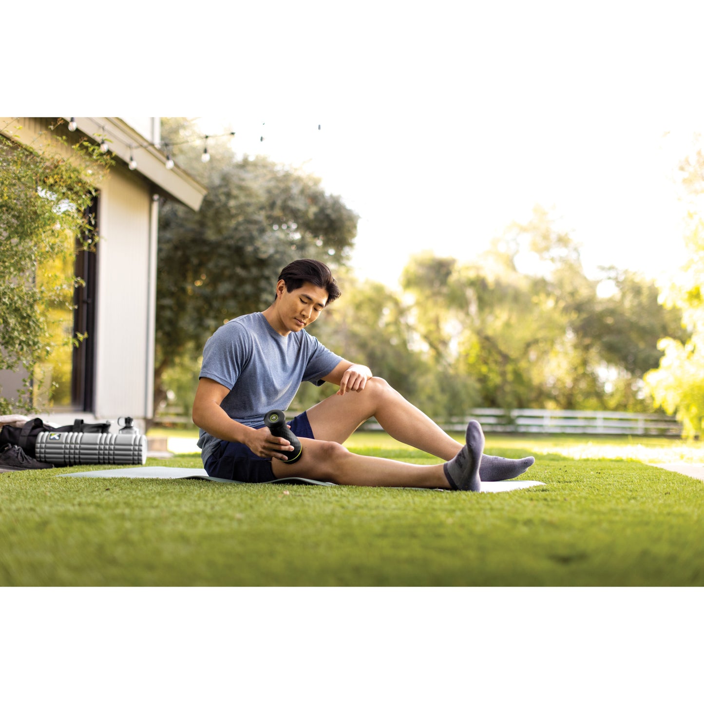 Man stretches leg with massage roller on grass in a backyard outdoor setting