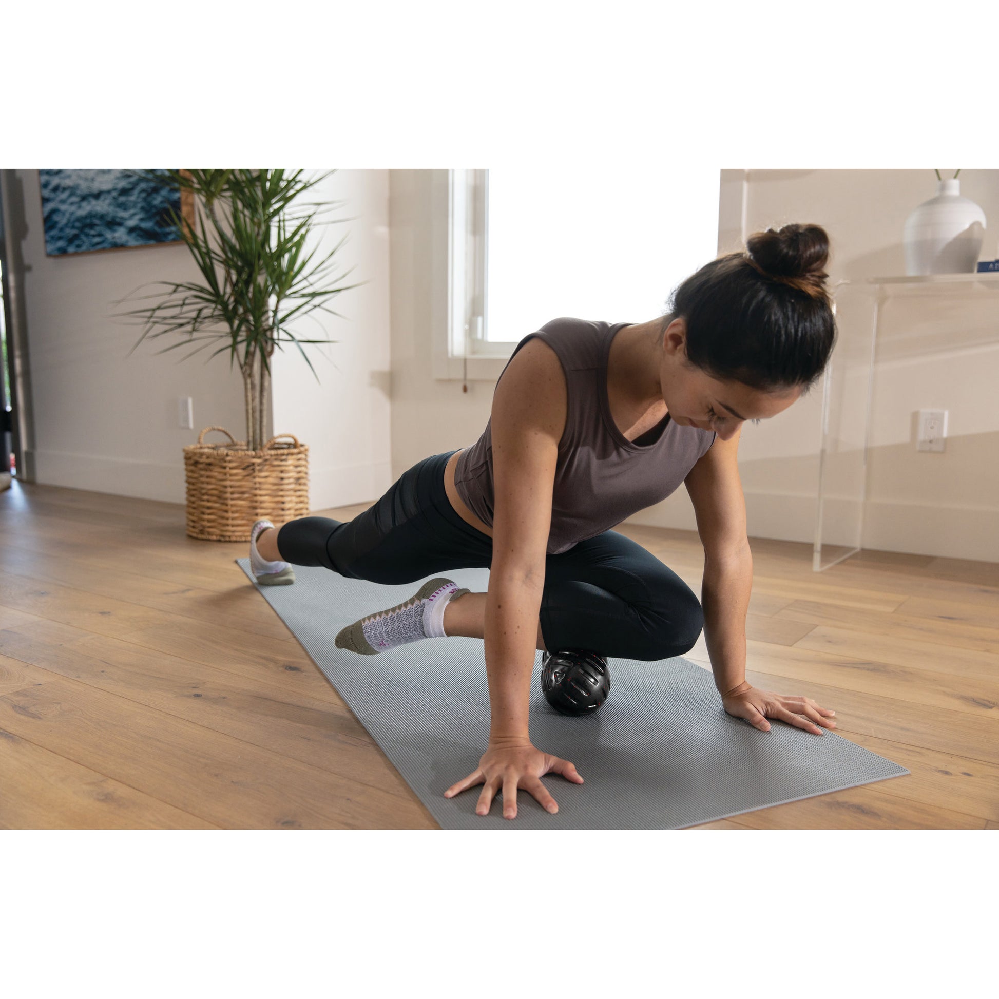 Woman uses a massage ball to exercise on a yoga mat in a living room.