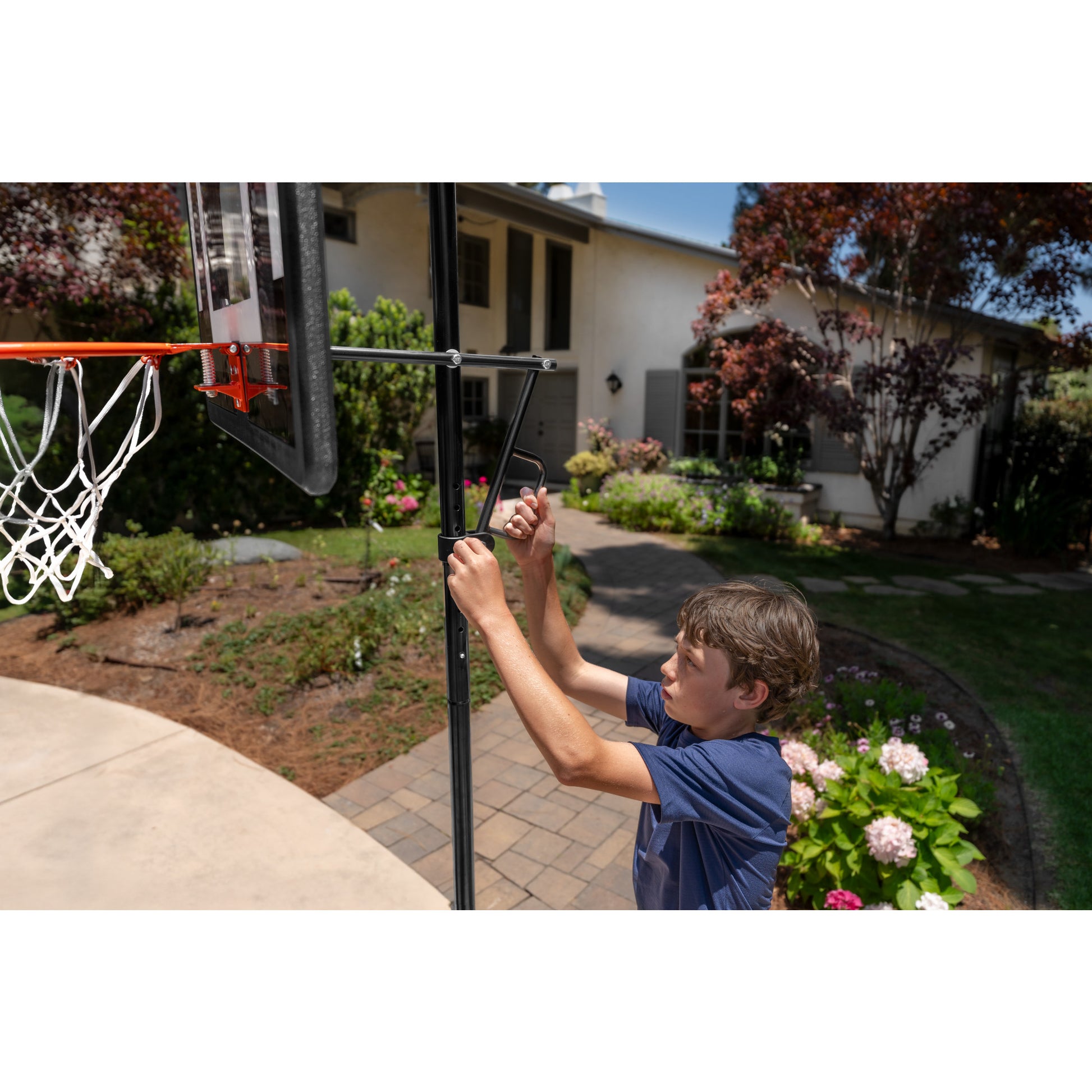 Boy installs basketball hoop on outdoor pole in a garden yard