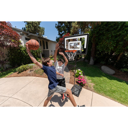 Two children play basketball on an outdoor court near a house and garden