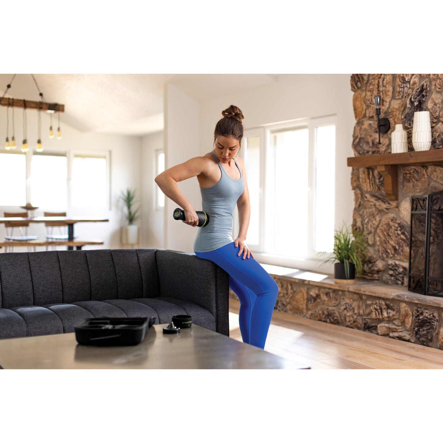 Woman exercises with dumbbell on couch in bright living room.