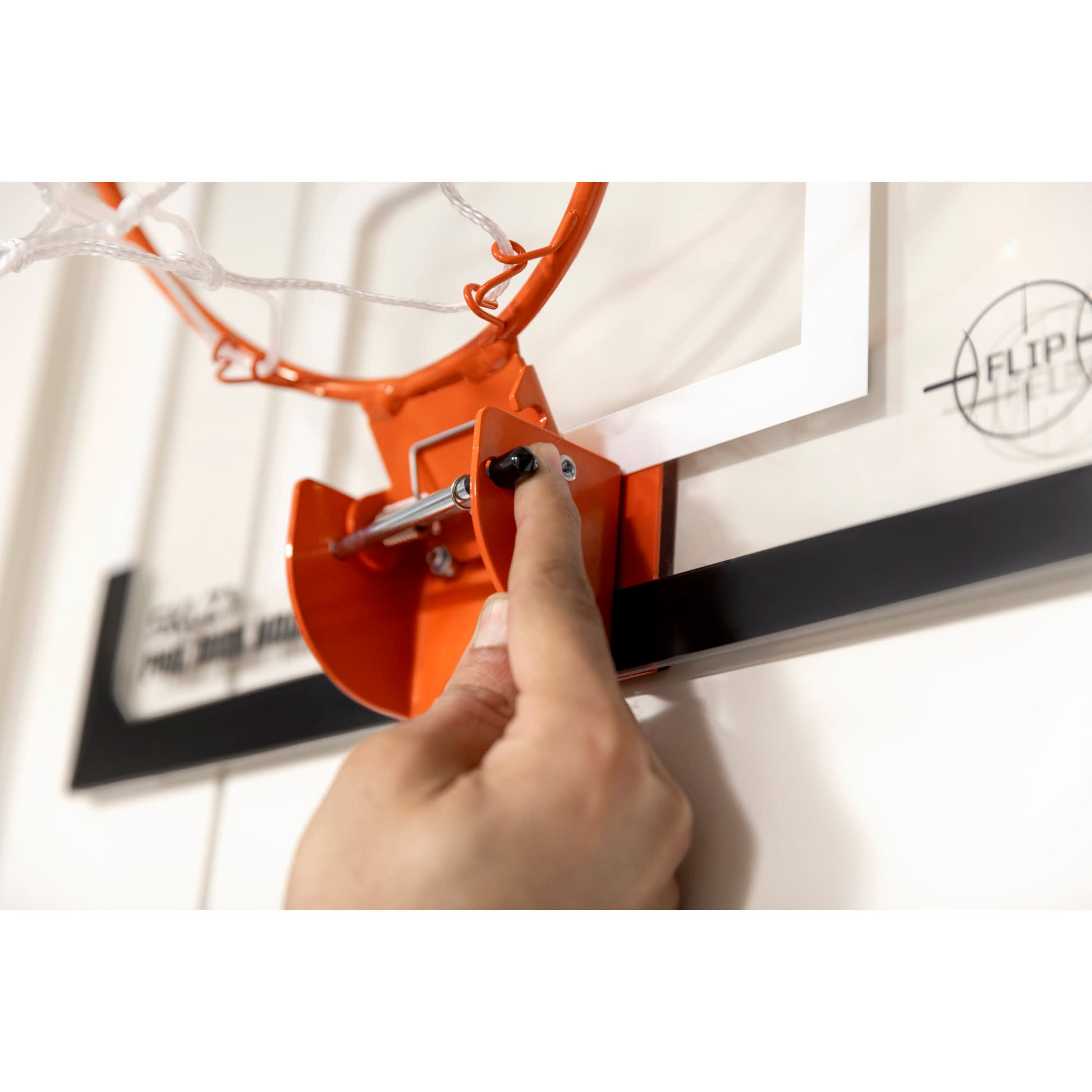 A hand adjusts a basketball hoop on a wall in a gymnasium.