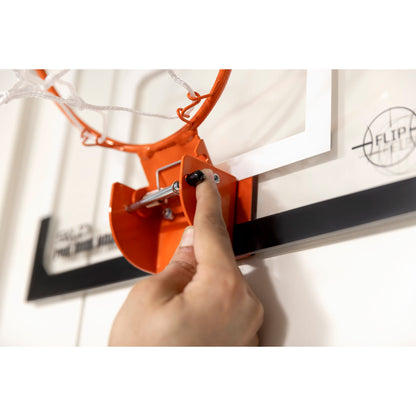 A hand adjusts a basketball hoop on a wall in a gymnasium.