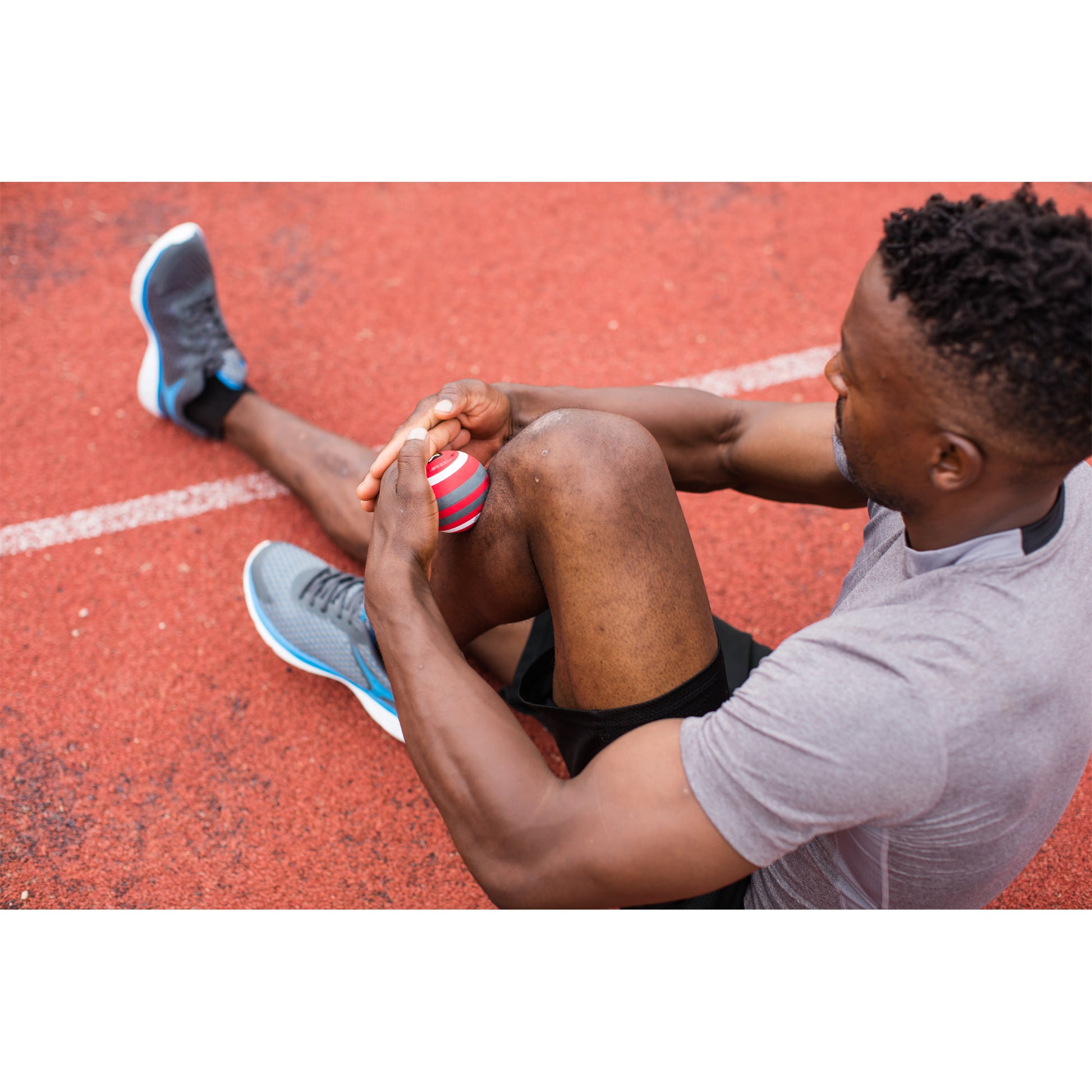 Athlete sitting on a running track holding a coach shot with a injured knee in sportswear