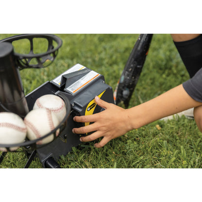 Child activates a pitching machine on the grass field for baseball practice.