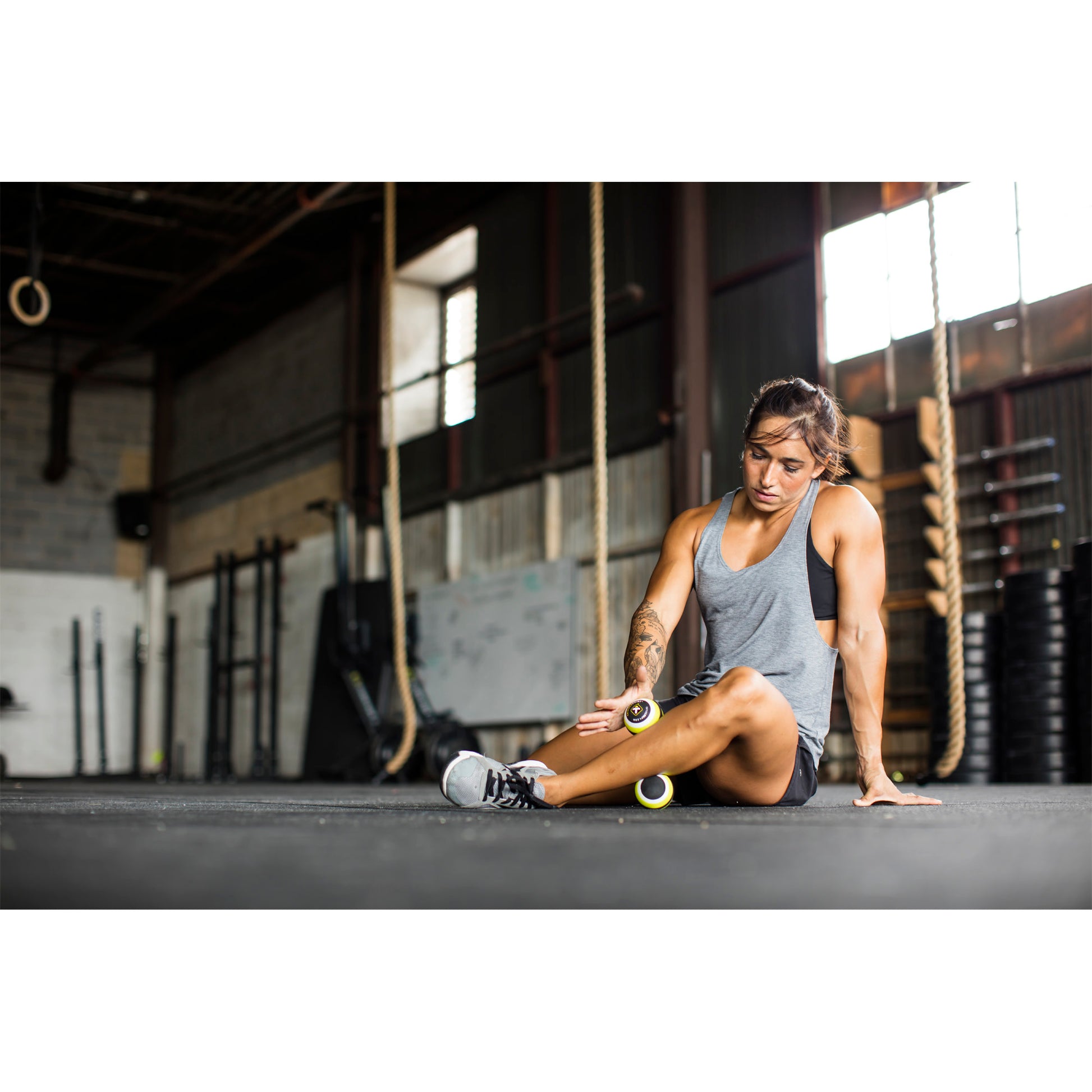Woman using foam roller to stretch thigh in gym environment