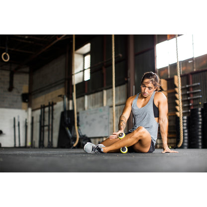 Woman using foam roller to stretch thigh in gym environment