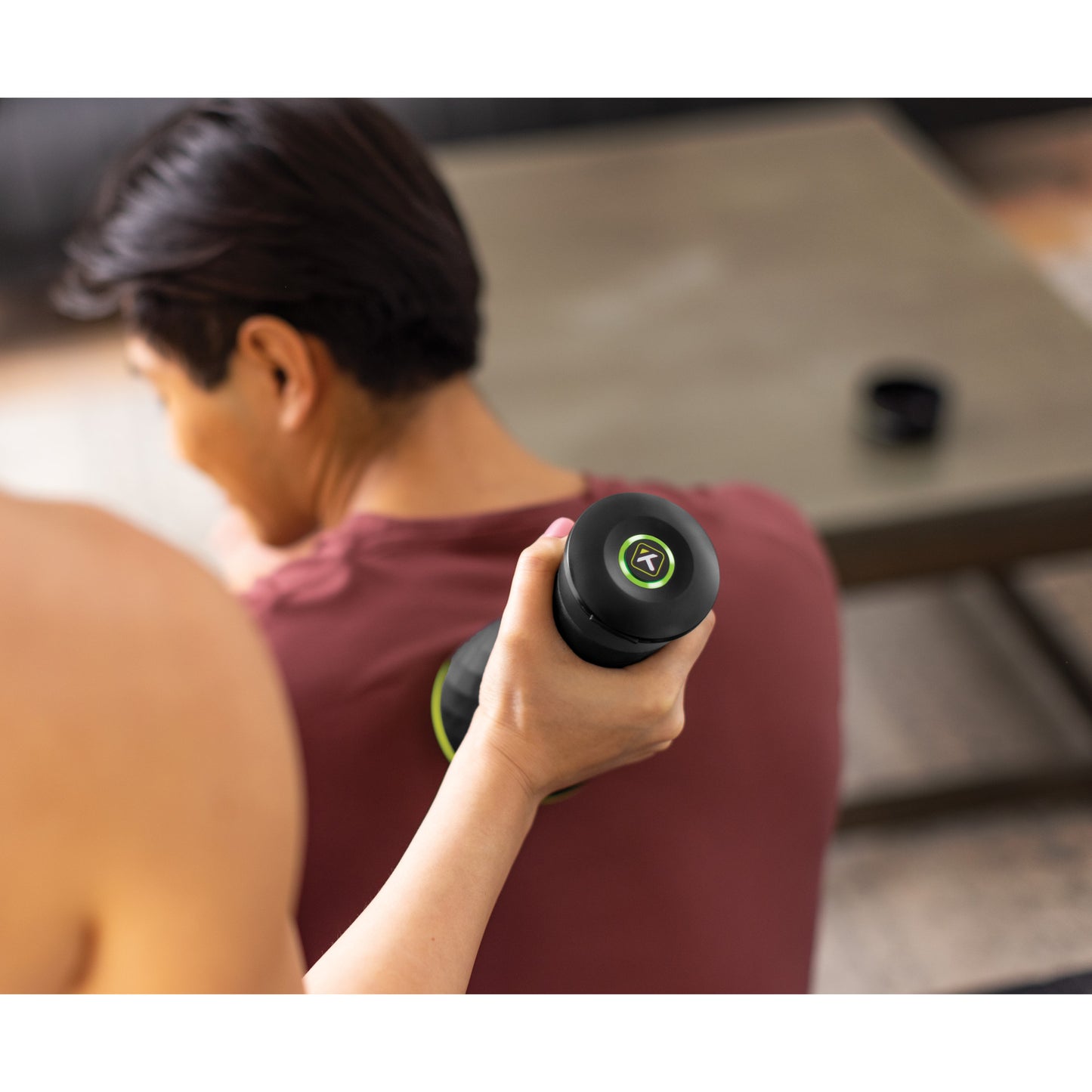 Person massages back with handheld device in a room with a table in the background.