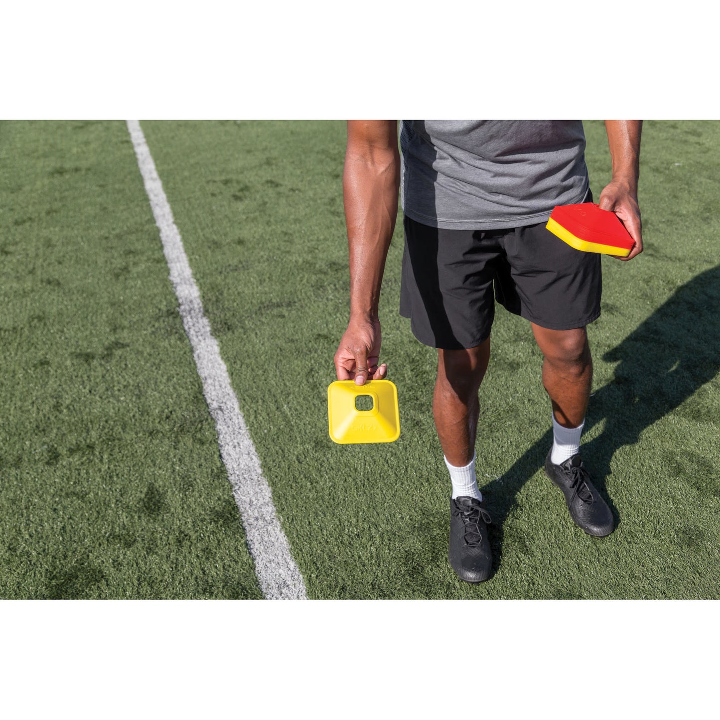 Person holds a yellow timer and a red paddle on a soccer field during training