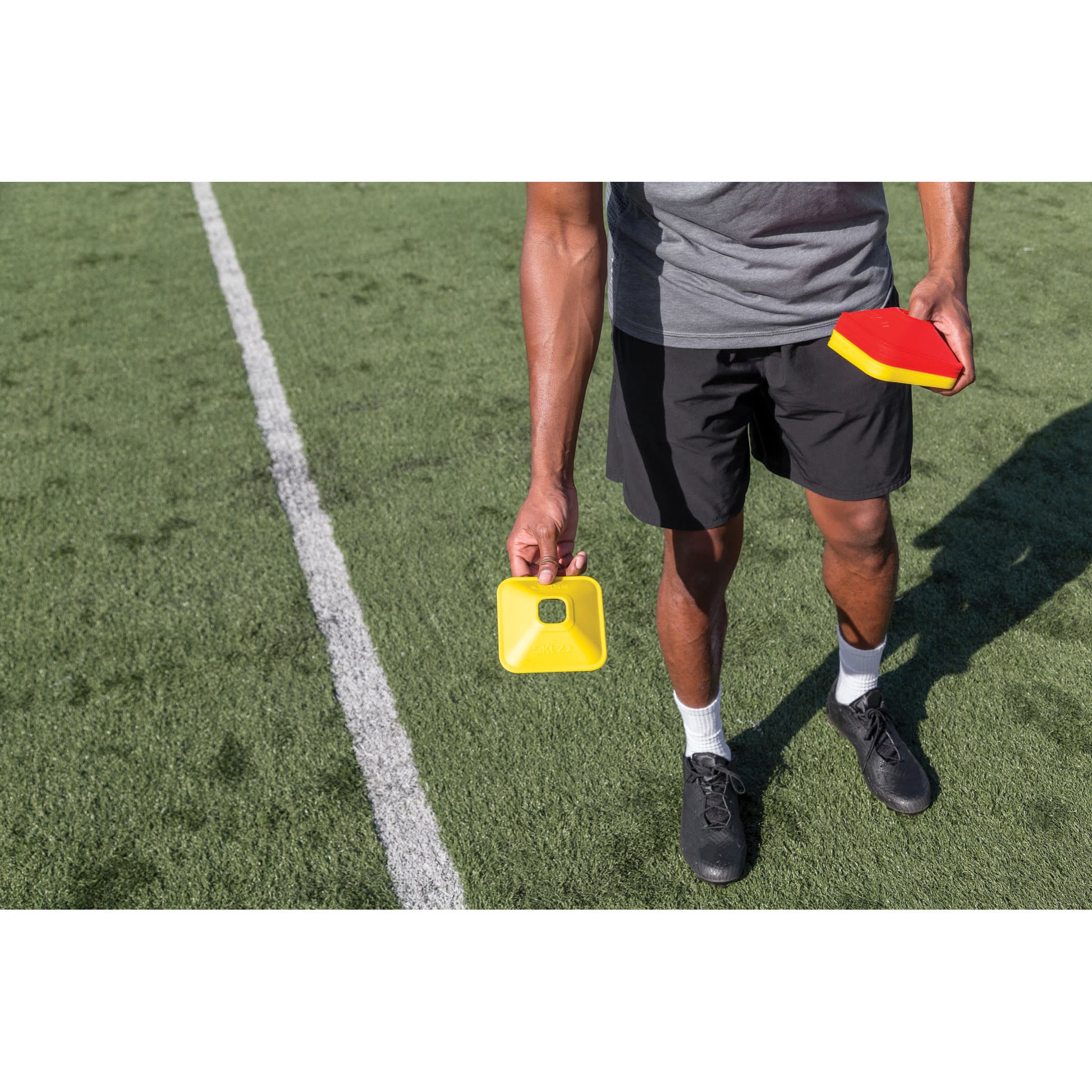 Person holds a yellow timer and a red paddle on a soccer field during training