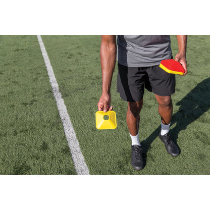 Person holds a yellow timer and a red paddle on a soccer field during training