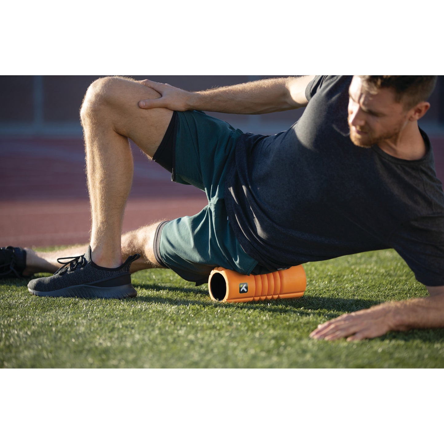 Man exercises with foam roller on field during outdoor workout session