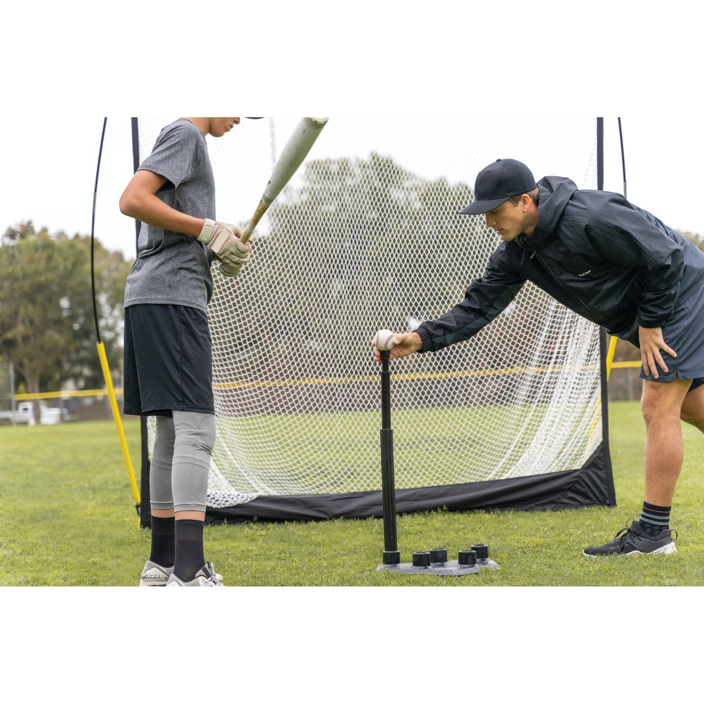 Shot of Coach placing ball on SKLZ 5-position tee for a male athlete on a field
