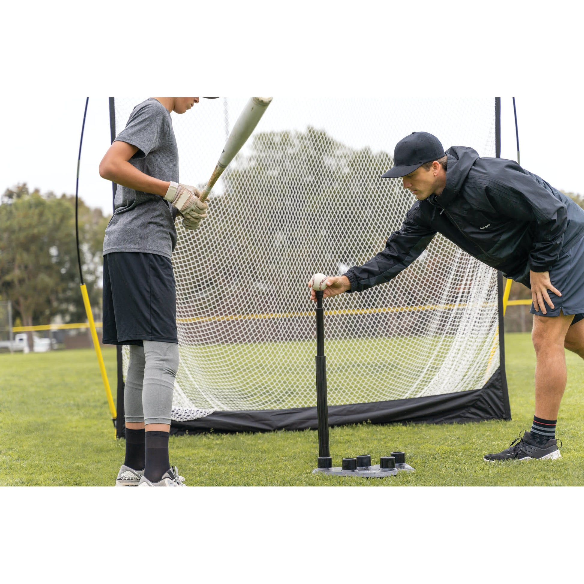 Shot of Coach placing ball on SKLZ 5-position tee for a male athlete on a field