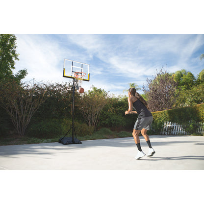 A woman shoots a basketball on an outdoor court in a sunny garden setting