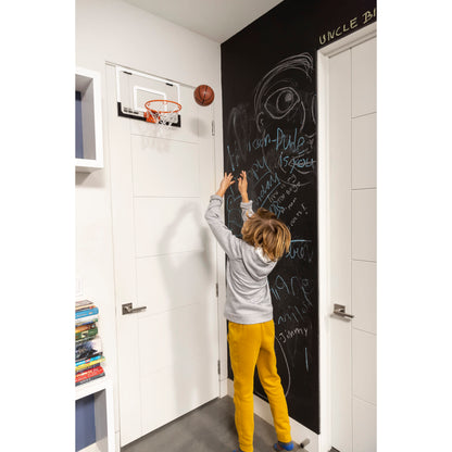 Child writes on chalkboard wall in a room with a basketball hoop and bookshelf