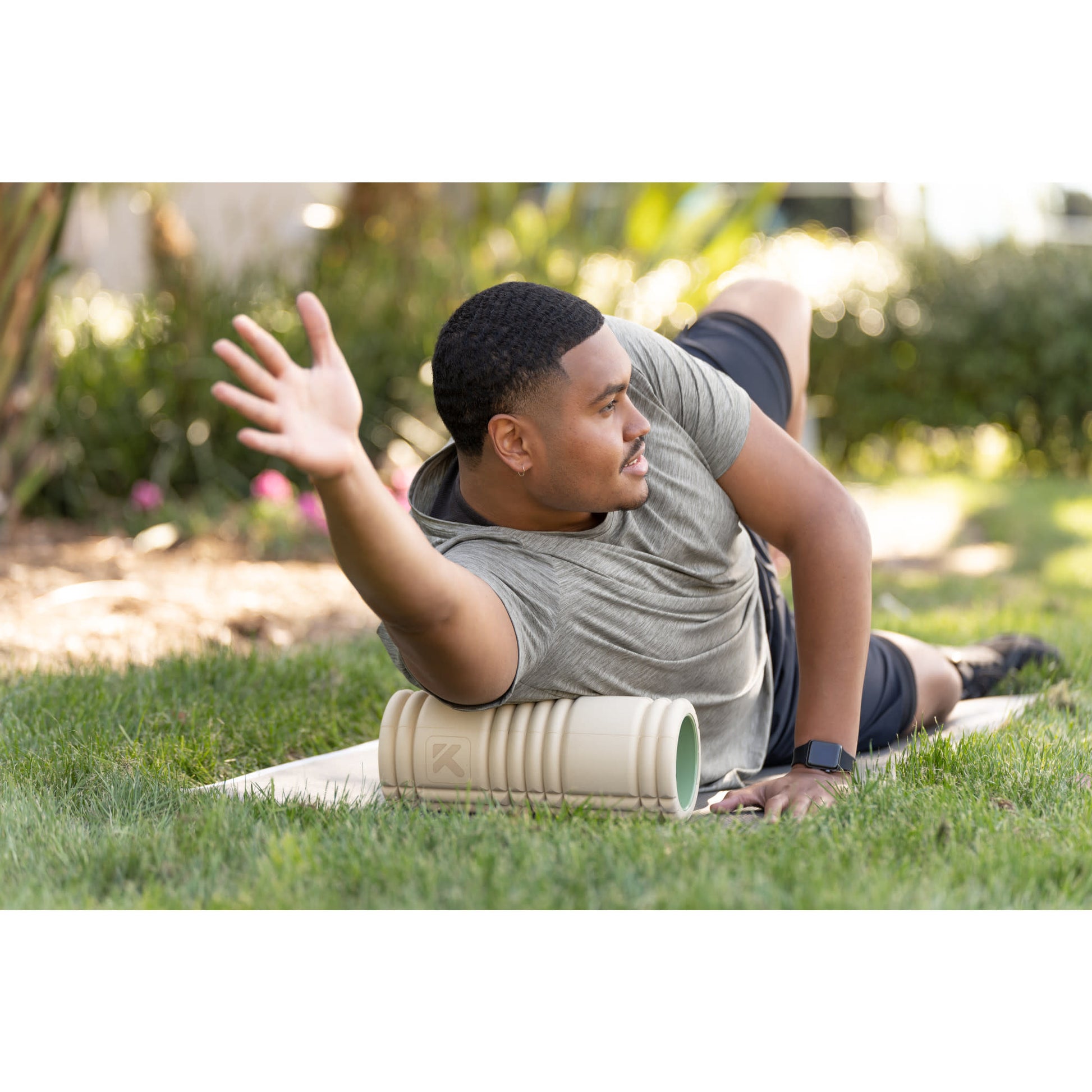 Man exercises outdoors using a foam roller on the grass in a garden setting.