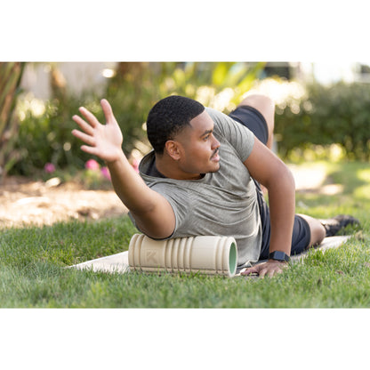 Man exercises outdoors using a foam roller on the grass in a garden setting.