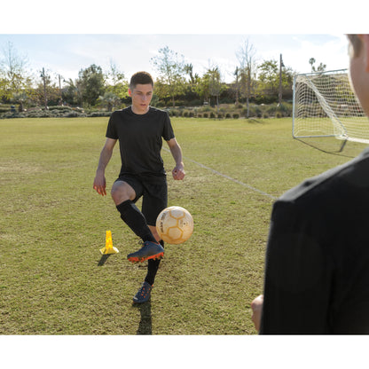 Young soccer player practicing dribbling on a grass field with a coach watching.