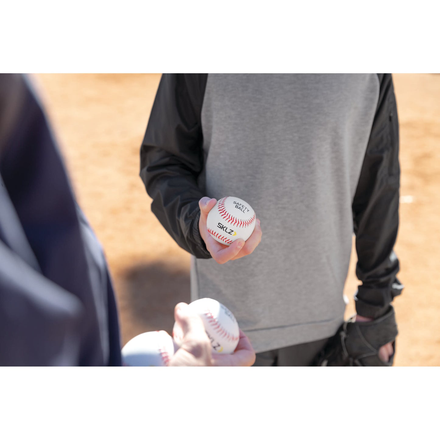 Person holds a baseball while another person offers additional balls on a baseball field.