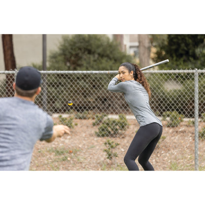 Girl with a bat prepares to swing in a fenced outdoor area during daytime