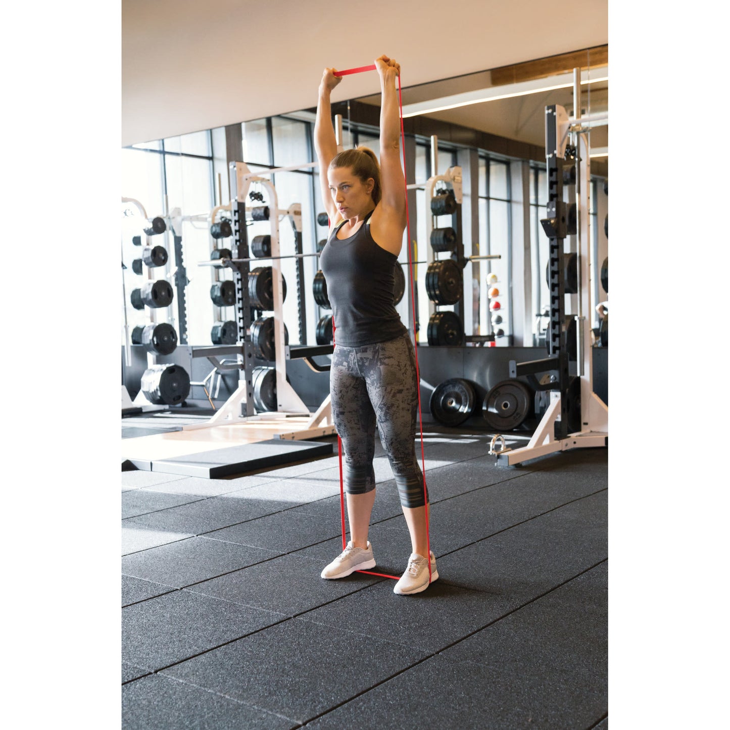 Woman with resistance band exercises in gym on black flooring with weight racks background
