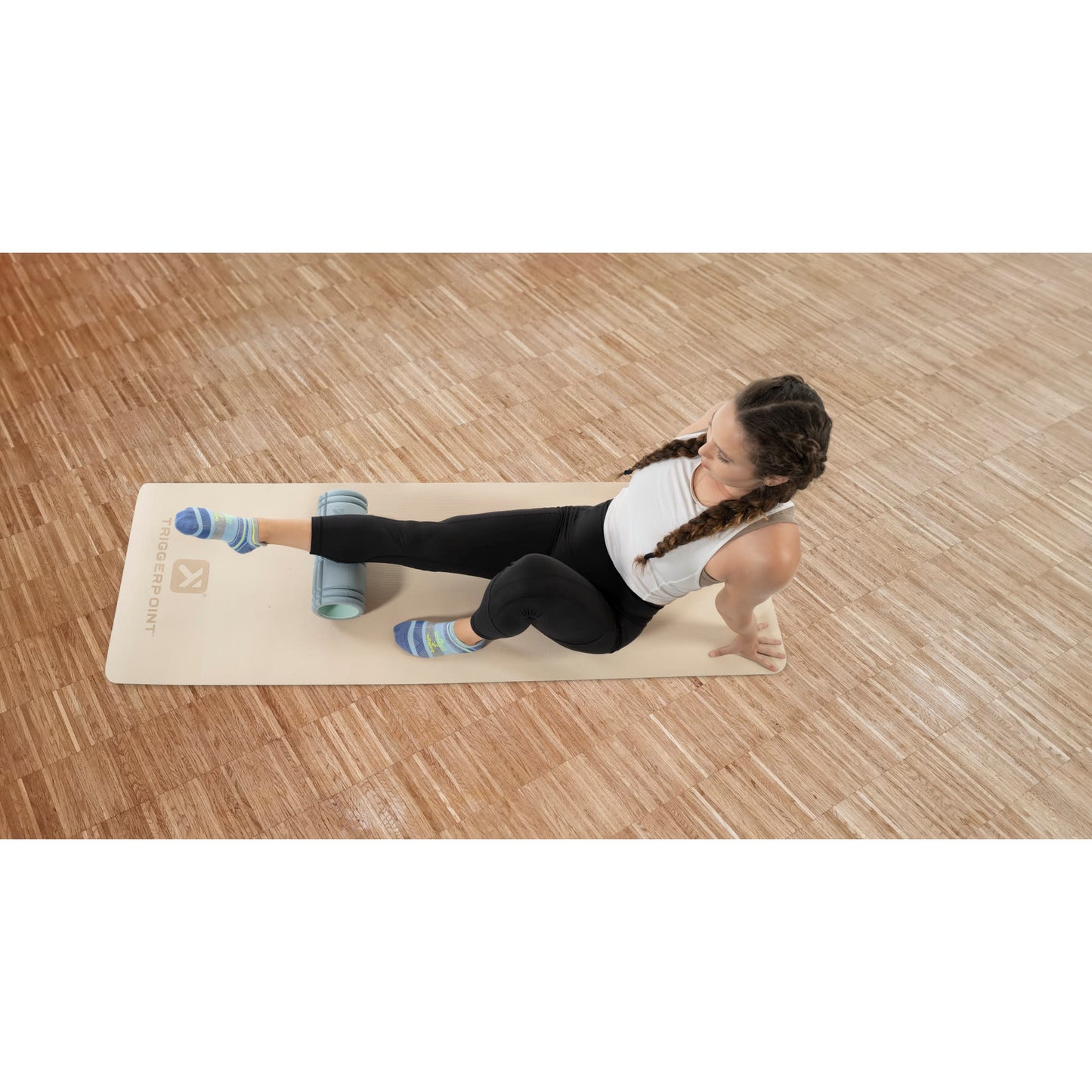 Woman performs leg stretch using foam roller on a yoga mat in a gym or studio.