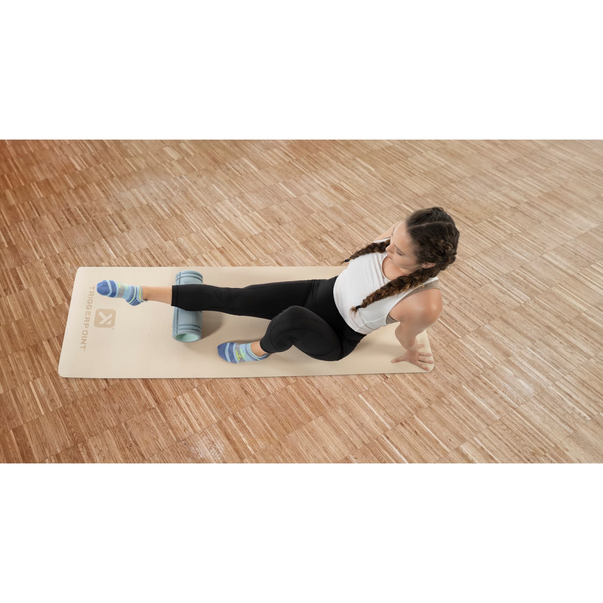 Woman performs leg stretch using foam roller on a yoga mat in a gym or studio.