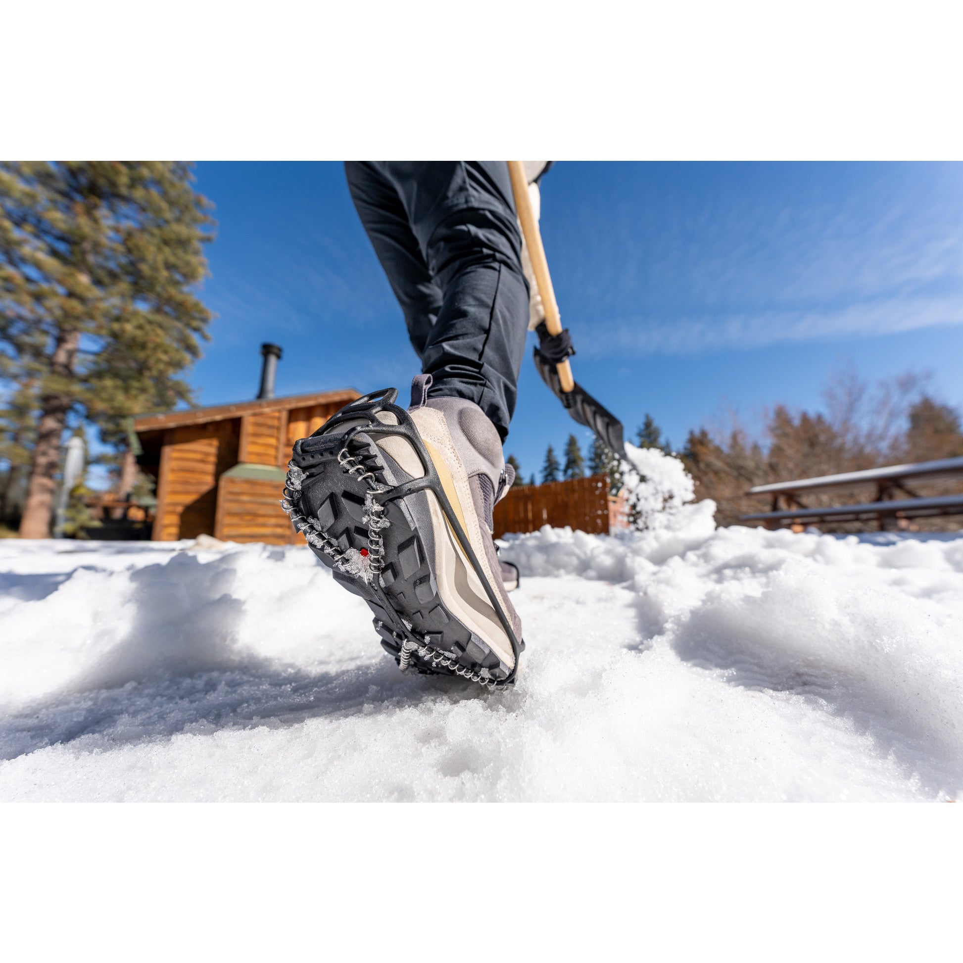 Person walks in snow using hiking shoes near a cabin in a winter landscape